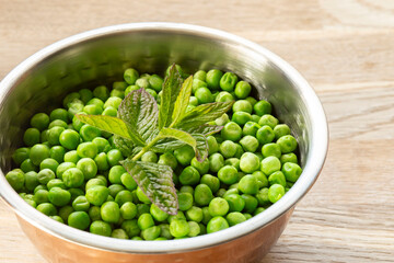 Petits pois peas in a capper serving bowl with freshly picked mint garnish. On a wooden cutting board.
