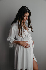Fototapeta premium Pregnant girl with white t-shirt and jeans on light background stroking belly
