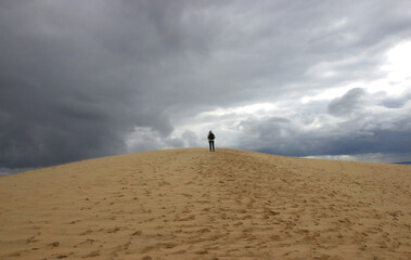 Under a stormy sky on a late April afternoon, a walker climbs the Dune du Pilat (Landes de Gascogne - France)