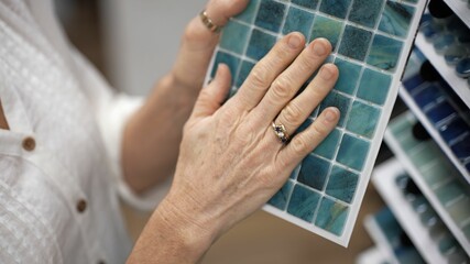 Obraz premium Closeup of hand touching glass wall tiles while shopping through samples for home redecorating renovation project, in a hardware store.