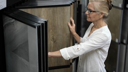 Happy mature woman touching luxury vinyl tile plank samples in a floor store for a home remodeling renovation project.