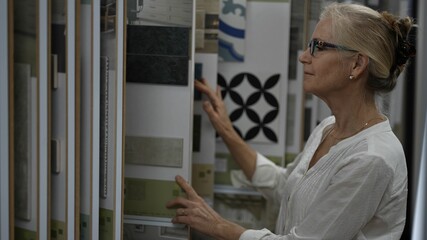 Happy mature woman looking through display of sample ceramic wall and floor tiles while shopping for home redecorating renovation project, in a home decorating store.