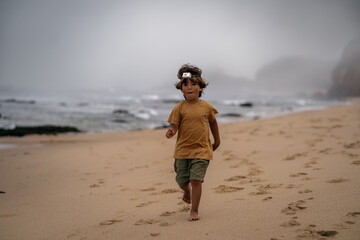 cute happy boy in a headlamp running fast on the beach with the background of the sea in the fog © Vadim
