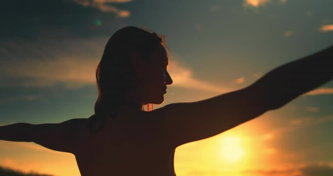 Woman silhouette against sunset seascape bright orange sky. Girl close up raises hands ang enjoy beautiful nature landscape. Outdoor lifestyle travel on summer holiday vacation. Slow motion back view