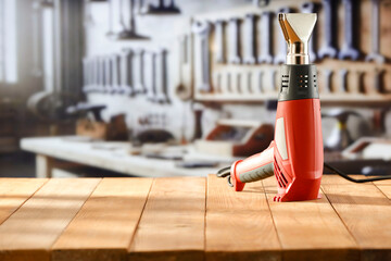 Heat gun tool on wooden work table in craft workshop. Blurred wall with tools in the background. Advertising space free for product mounting
