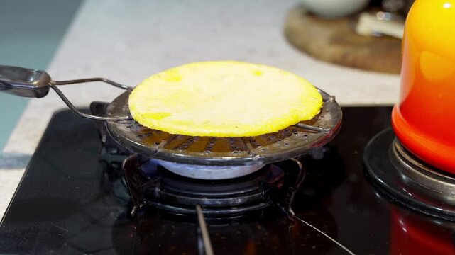 Making Arepas: Traditional Cooking. Hands roast an arepa on a stove using a frying pan, demonstrating the traditional method of preparing this popular Latin American dish