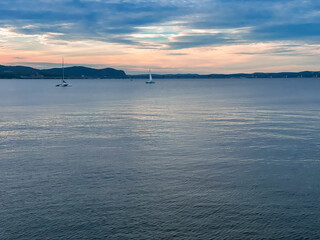 Piermont, NY - US - June 28, 2024 a tranquil evening over the Hudson River, with sailboats gently floating on calm waters and a backdrop of hills under a soft, pastel sky.