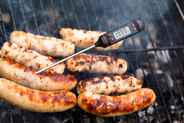 Close-up shot of digital meat thermometer with Fahrenheit scale showing safe cooking temperature inside of grilling turkey sausages on smoking barbecue