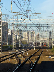 Detailed view of modern railway tracks and overhead power lines with a train approaching in a city setting.