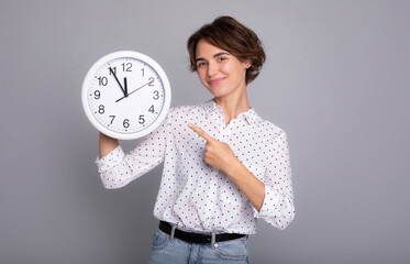 Portrait of beautiful pretty young business woman having clock in hands looking at camera isolated on grey color background studio.