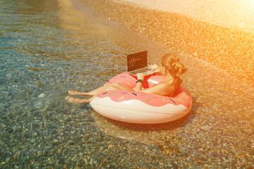 Woman laptop sea. Freelancer woman in sunglases floating on an inflatable big pink donut with a laptop in the sea. People summer vacation rest lifestyle concept