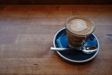 A beautifully crafted latte with intricate foam art in a glass cup, set on a dark blue saucer with a silver spoon.