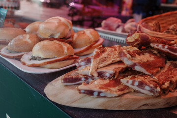 A close-up view of freshly made pork belly sandwiches and sliced pork belly on display at a market or deli.