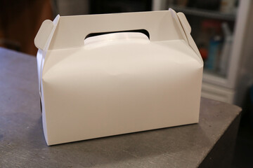 white plain cardboard favor box with handle on concrete kitchen table gable cupcake carrier dessert carrying package blank mock up
