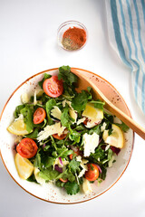 Summer salad with cherry tomatoes, baked pepper, salad mix, lemon and  arugula,  topped with parmesan cheese. Keto diet, healthy food. Light grey stone background. Top view.