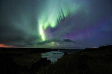 Long exposure of the Aurora Borealis above a beach in the Icelandic Westfjords with a starry sky.