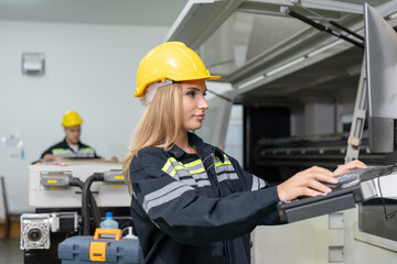 Engineer female operating cutting cardboard box machine in paper factory. Woman technical in uniform wearing helmet safety monitor and setting program in laser CNC cutting