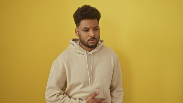 Young african american man wearing hoodie with hand on stomach because nausea, painful disease feeling unwell. ache concept. over isolated yellow background
