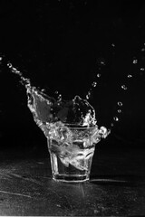 Ice splashing into a glass of water on a black background