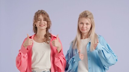 Young stylish women models smiling showing thumbs up like gesture, isolated on purple background. Fashion and youth beauty concept.