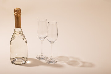 A bottle of white sparkling wine in two glasses on a beige background. Copy space