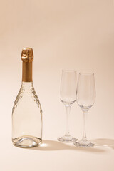 Bottle of white sparkling wine two glasses on a beige background.