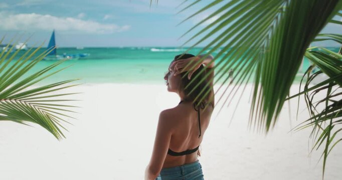 A woman stands confidently on the white sandy beach of Boracay Island in the Philippines, enjoying the sun and sea in her bikini attire.