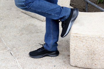 Adult man wears black sneakers to walk down the city street, ties his shoelaces, a new way to dress casually for work