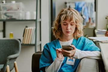 Medium close up of Caucasian doctor sitting on sofa and replying her patient via smartphone while...