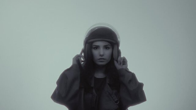 A young attractive girl puts on a helmet. A beautiful woman in a leather jacket puts on a plastic protective helmet for a motorcycle or scooter. Urban lifestyle. Independent and strong girl, feminism