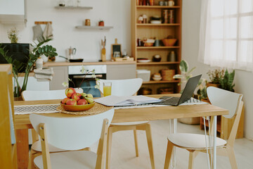 Huge light modern kitchen full of brand new furniture, wooden table with laptop and bowl with healthy snacks