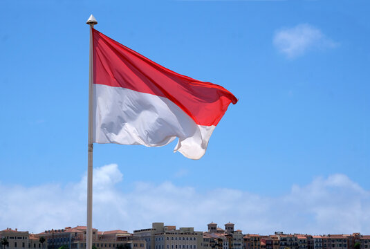 The flag of Monaco waving in the wind in front of a blue sky