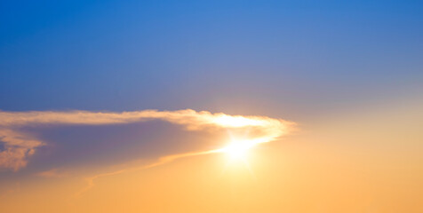 Sunset sky with sun behind cloud and rim light on beautiful majestic yellow and blue idyllic evening sky background in panoramic view
