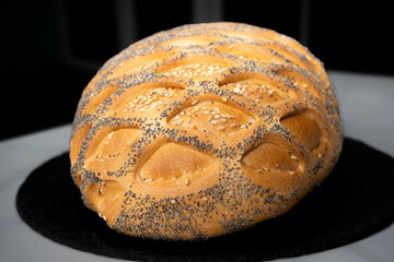 Beautiful freshly baked oval bread with poppy and sesame seeds on the table on a black base. Fragrant, delicious bread with a crispy crust. Close-up.