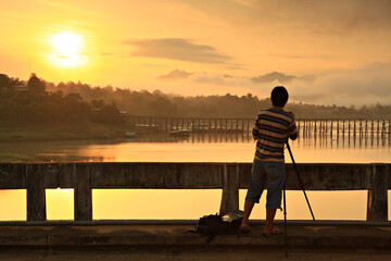 Fototapeta premium A Photographer take picture Wood bridge with river and mountain in Sangkhla buri, Kanchanaburi province, Thailand 