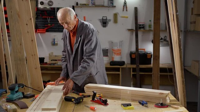 Craftsman and DIY handmade. Elderly man carpenter with wooden planks in carpentry workshop, furniture manufacture.