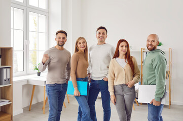 Obraz premium Group of young people men and women looking at camera and smiling standing at office. Employees team, company staff or a group of students standing in a row confidently and cheerfully.
