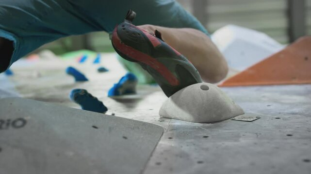 Bottom view: A sporty Caucasian man climbs a bouldering wall. Moves legs on ledges. Practices climbing on an artificial indoor wall. Extreme sports, active lifestyle. Training on the climbing wall.