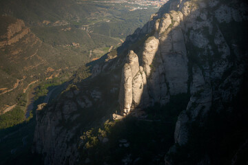 Colossal monolithic stone formations lit by the last rays of the sun before dusk on Montserrat mountain on the Iberian Peninsula. Artistic photography with a fantasy and mystery ambience