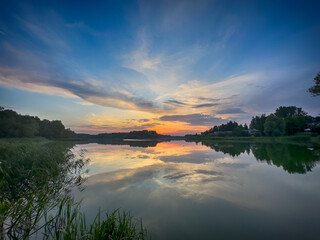 Serene Fishing Lake: A peaceful scene by the tranquil waters of a secluded fishing lake. Surrounded by lush greenery and framed by a clear blue sky, this picture captures the essence of a perfect day 