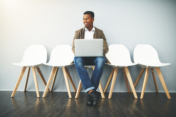 Man, laptop and happy for interview on chair by wall, thinking or mockup space for job opportunity. African person, computer and queue with resume, human resource or waiting at recruitment agency
