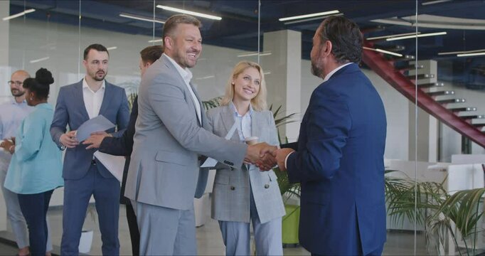 Smiling office workers shake hands and get to know each other at briefing during coffee break. Male and female colleagues greet each other and discuss work. Business cooperation concept.