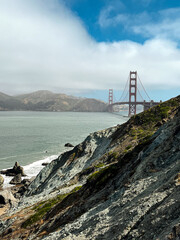 Coastal view of the Golden Gate bridge in San Francisco. American iconic landmark. Cliffs and grass frame the picture. Waves in the bay water. Light fog.