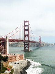 Coastal view of the Golden Gate bridge in San Francisco. American iconic landmark. Cliffs and grass frame the picture. Waves in the bay water. Light fog.