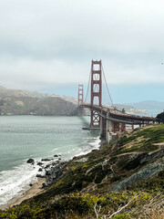 Coastal view of the Golden Gate bridge in San Francisco. American iconic landmark. Cliffs and grass frame the picture. Waves in the bay water. Light fog.