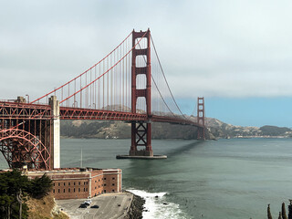 Coastal view of the Golden Gate bridge in San Francisco. American iconic landmark. Cliffs and grass frame the picture. Waves in the bay water. Light fog.