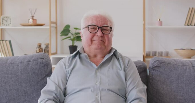 Senior man greets doctor online, indicating pain in head and heart and asks for prescription. Man in need of treatment is sitting on sofa in front of web camera and talking to doctor via video call.