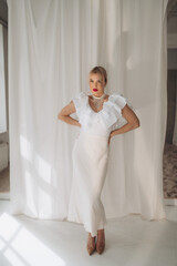  Elegant woman with blonde bob haircut and red lipstick posing confidently in a white ruffled dress...