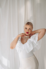 Elegant woman with blonde bob haircut and red lipstick posing with hands on her neck in a white...