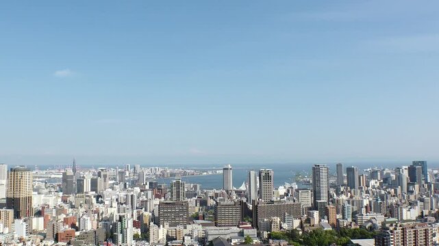 KOBE, HYOGO, JAPAN - JUNE 2024 : Aerial high angle view of Kobe city and Kobe port in daytime. View of buildings and street around Kobe port tower and Sannomiya station. 4K time lapse shot.